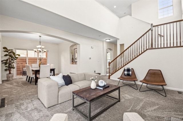 carpeted living area featuring arched walkways, a chandelier, a towering ceiling, baseboards, and stairs