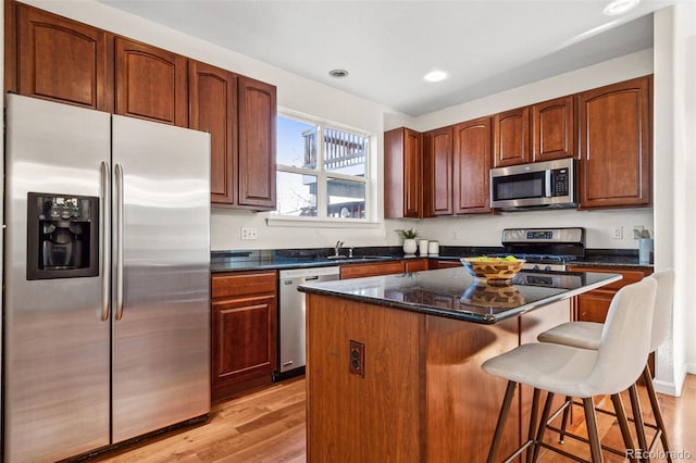 kitchen with a breakfast bar, stainless steel appliances, light wood-style flooring, a kitchen island, and a sink