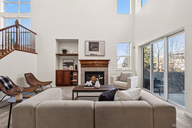 carpeted living room with baseboards, built in shelves, a high ceiling, and a tile fireplace