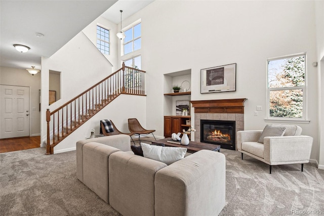 carpeted living area featuring baseboards, a high ceiling, stairway, and a tiled fireplace