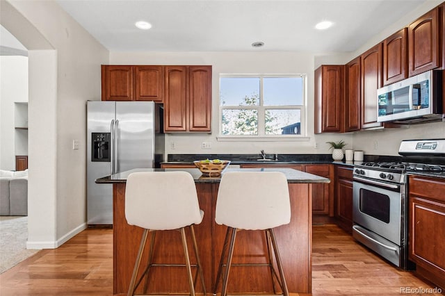 kitchen with dark countertops, appliances with stainless steel finishes, a breakfast bar, a center island, and light wood-type flooring