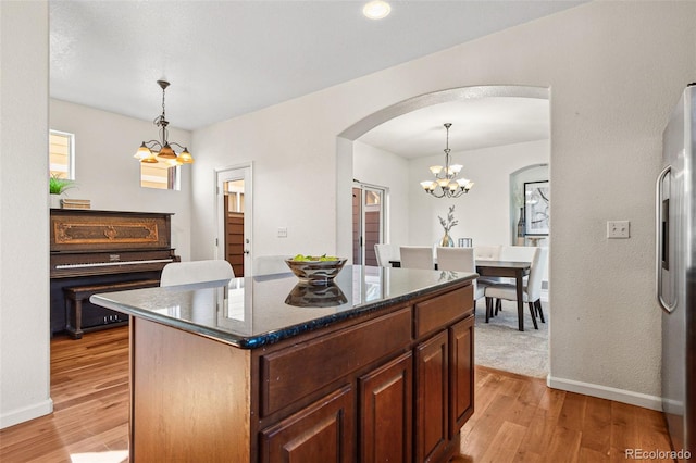 kitchen with a center island, arched walkways, freestanding refrigerator, a chandelier, and light wood-type flooring