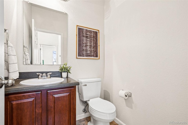 half bathroom with vanity, toilet, and baseboards