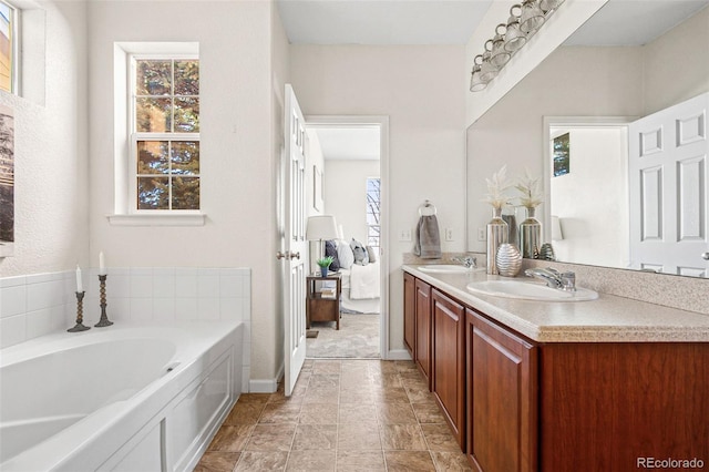 ensuite bathroom with double vanity, a healthy amount of sunlight, a sink, and a bath