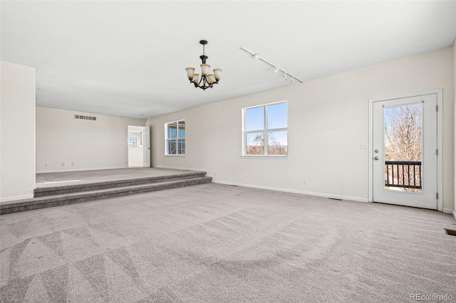 carpeted spare room with a chandelier, baseboards, visible vents, and track lighting