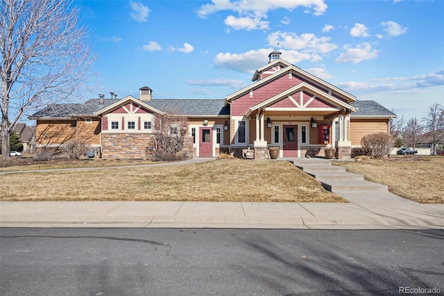 view of front facade with covered porch, a front yard, and stone siding