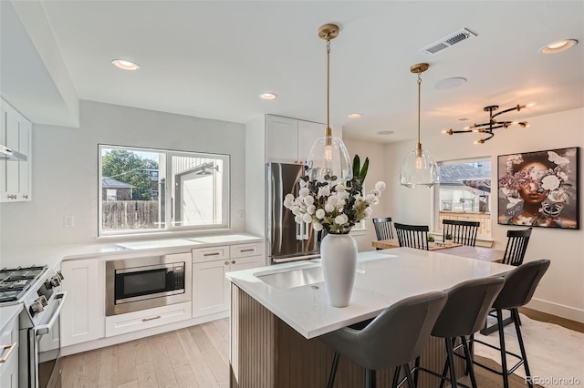 kitchen with appliances with stainless steel finishes, light hardwood / wood-style floors, pendant lighting, white cabinets, and a chandelier