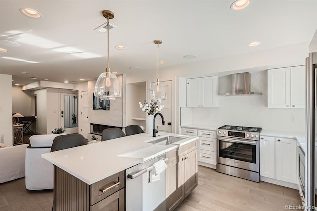 kitchen featuring white cabinetry, wall chimney range hood, stainless steel appliances, and a kitchen island with sink