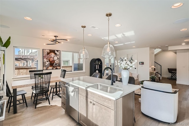 kitchen featuring sink, hanging light fixtures, light hardwood / wood-style flooring, an island with sink, and a chandelier