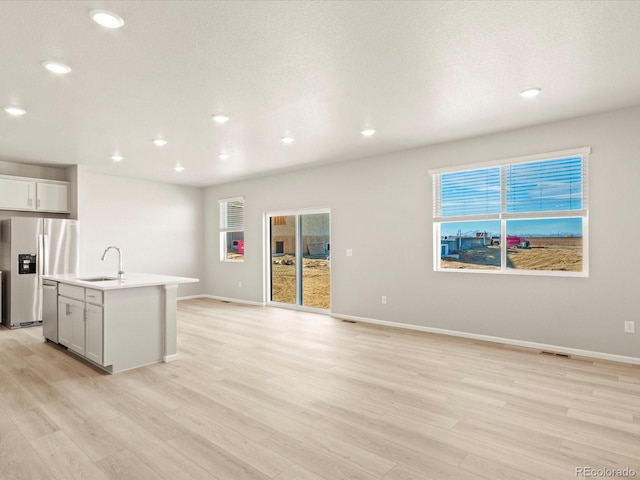 kitchen featuring sink, appliances with stainless steel finishes, a kitchen island with sink, and light wood-type flooring