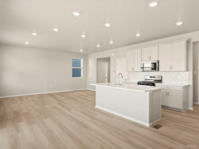 kitchen with white cabinetry, stainless steel appliances, sink, a kitchen island with sink, and light wood-type flooring