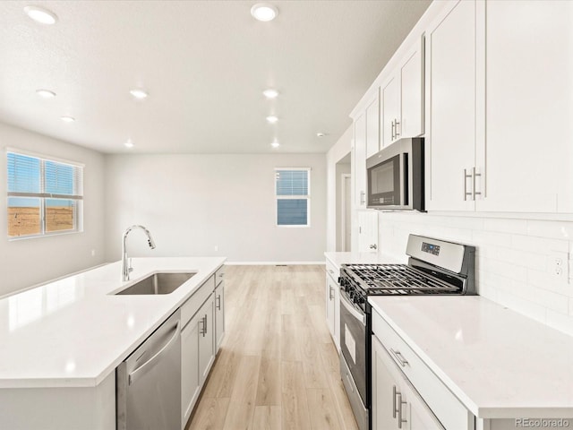 kitchen with appliances with stainless steel finishes, a kitchen island with sink, white cabinets, light hardwood / wood-style flooring, and sink