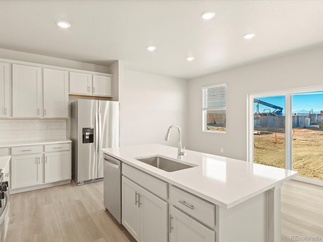 kitchen featuring white cabinetry, stainless steel appliances, decorative backsplash, sink, and a center island with sink