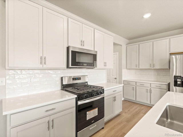 kitchen featuring backsplash, light hardwood / wood-style floors, sink, white cabinetry, and appliances with stainless steel finishes