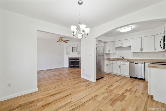 kitchen featuring white cabinetry, stainless steel appliances, pendant lighting, light hardwood / wood-style floors, and ceiling fan with notable chandelier