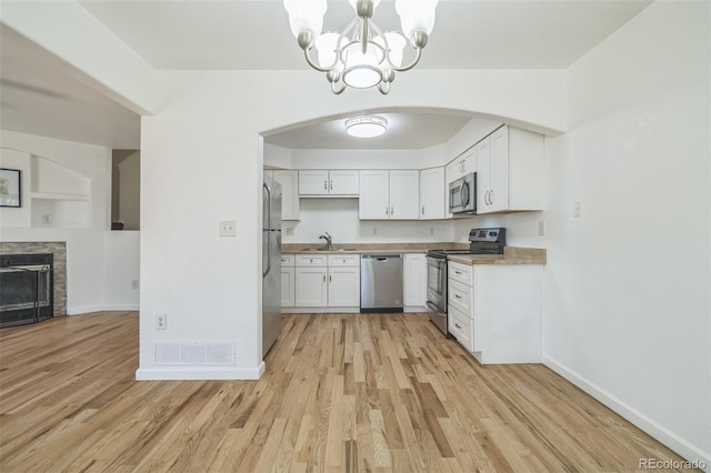 kitchen with a stone fireplace, sink, light wood-type flooring, appliances with stainless steel finishes, and white cabinetry