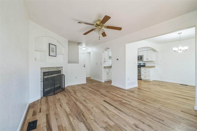 unfurnished living room with a stone fireplace, light hardwood / wood-style flooring, and ceiling fan with notable chandelier