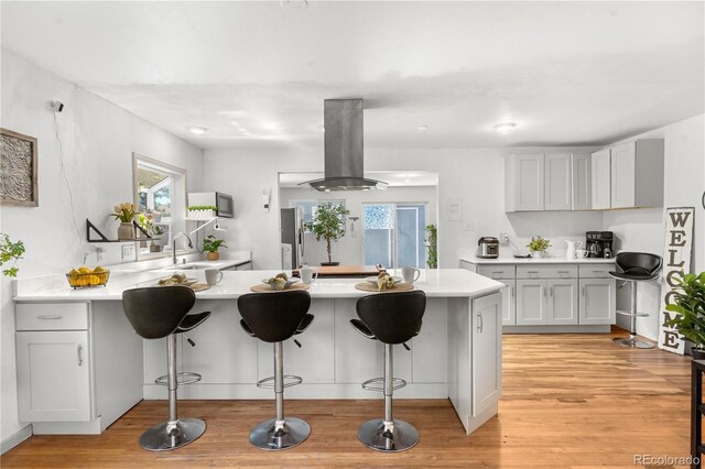 935 S Pecos Way, Denver, CO 80223 - kitchen featuring island exhaust hood, a peninsula, a breakfast bar area, and light countertops