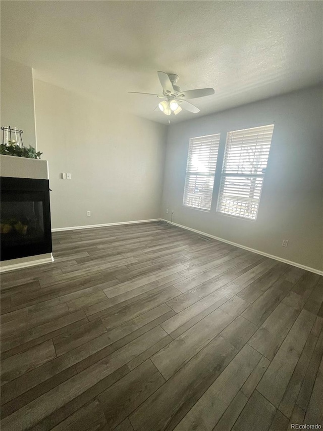 unfurnished living room with dark wood-style floors, ceiling fan, a glass covered fireplace, and baseboards