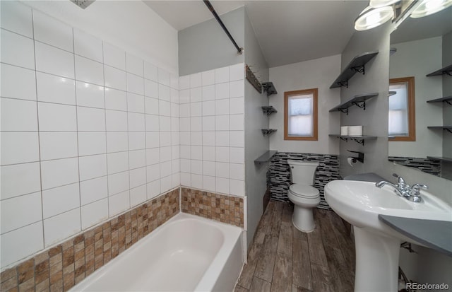 bathroom with hardwood / wood-style flooring, toilet, and tiled shower / bath