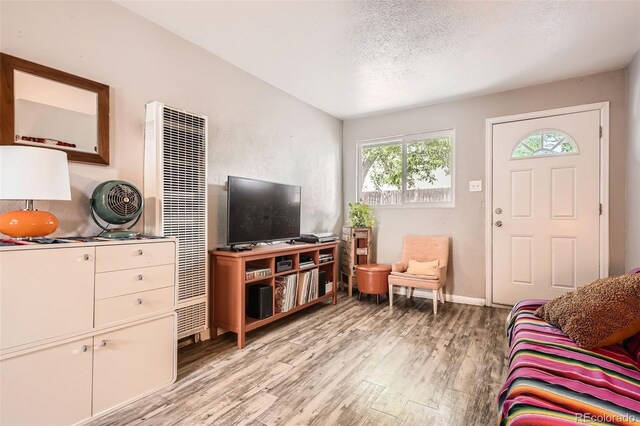 living area with a heating unit, light wood-type flooring, a textured ceiling, and baseboards