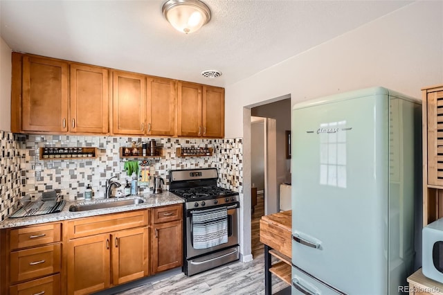 kitchen featuring stainless steel gas range, a sink, freestanding refrigerator, and brown cabinets