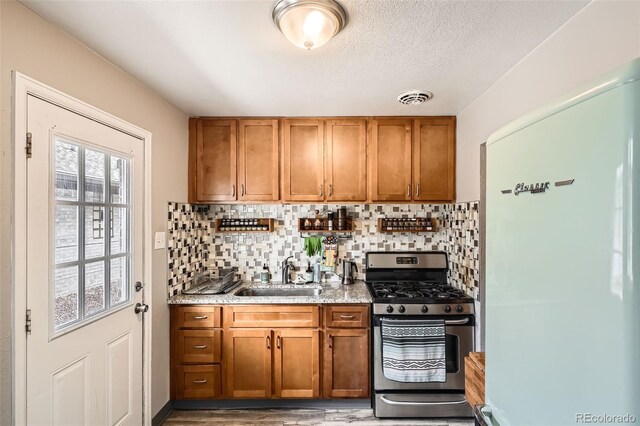 kitchen featuring freestanding refrigerator, stainless steel gas range oven, a sink, and brown cabinetry