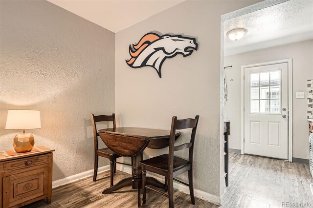 dining area with a textured wall, light wood-style flooring, and baseboards