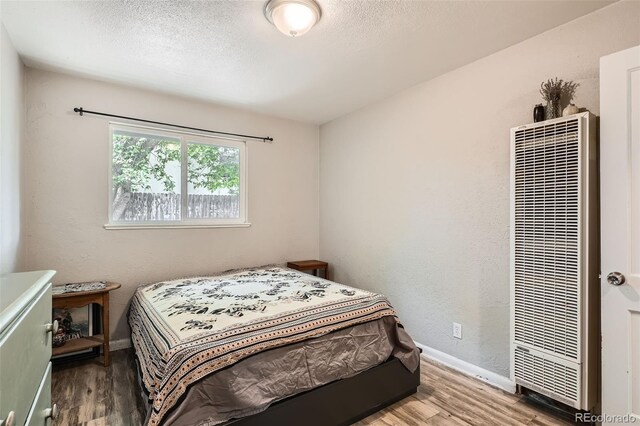 bedroom featuring a heating unit, wood finished floors, baseboards, and a textured ceiling
