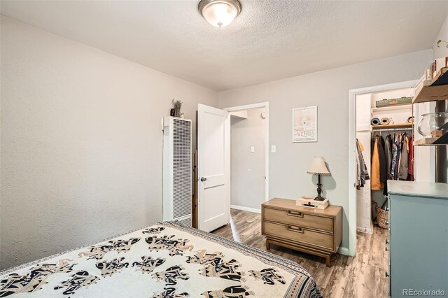 bedroom with a heating unit, a closet, a spacious closet, wood finished floors, and baseboards