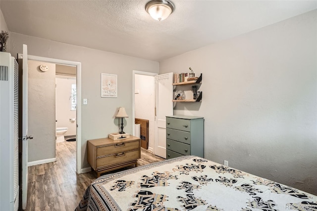 bedroom with light wood finished floors, baseboards, a heating unit, and a textured ceiling