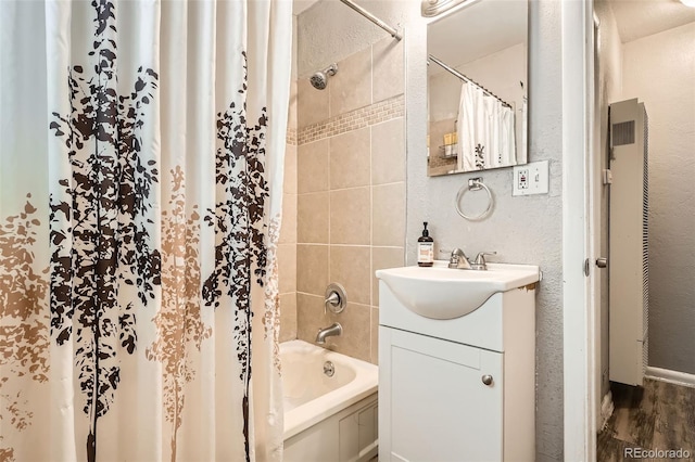 full bath featuring vanity, shower / tub combo with curtain, a textured wall, and wood finished floors
