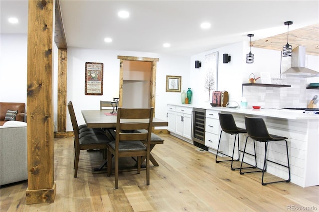 900 Tallaqua Dr, Grand Lake, CO 80447 - kitchen with wall chimney range hood, wine cooler, light wood-style floors, a kitchen bar, and light countertops