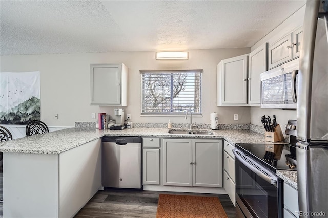 kitchen with a textured ceiling, dark wood finished floors, a sink, a peninsula, and stainless steel appliances