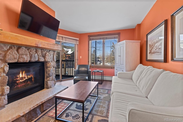 living area with a baseboard radiator, baseboards, a stone fireplace, and wood finished floors