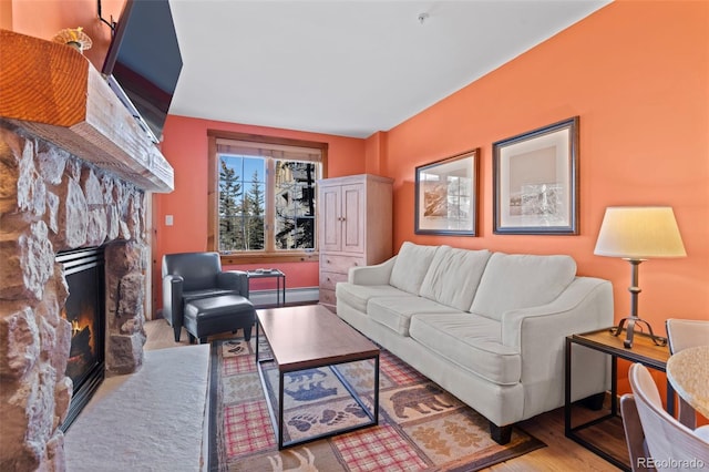 living area with a baseboard heating unit, a stone fireplace, and wood finished floors