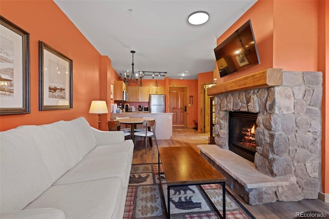 living room with rail lighting, a notable chandelier, a fireplace, and light wood-type flooring