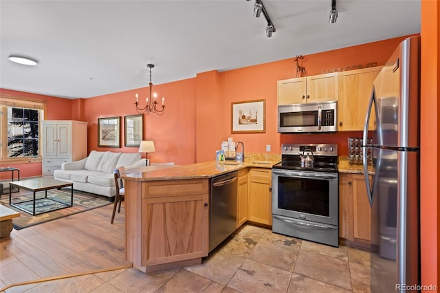 kitchen with light brown cabinetry, open floor plan, light stone counters, a peninsula, and stainless steel appliances