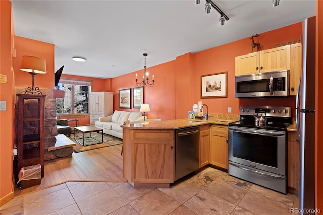 kitchen with light stone counters, light brown cabinets, a peninsula, appliances with stainless steel finishes, and open floor plan