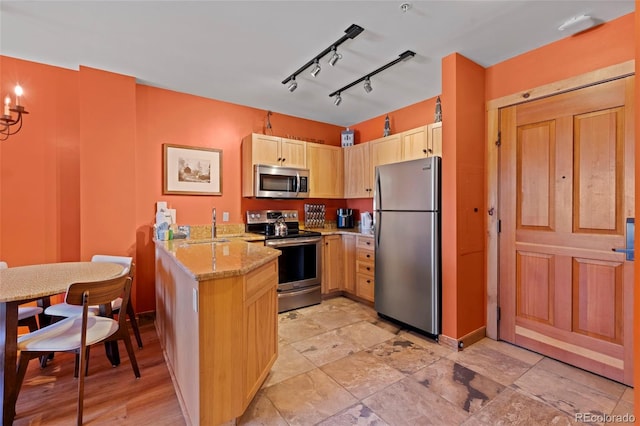 kitchen featuring light brown cabinets, baseboards, light stone countertops, a peninsula, and stainless steel appliances