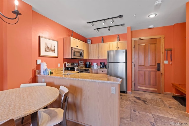 kitchen featuring a sink, light stone countertops, appliances with stainless steel finishes, and a peninsula