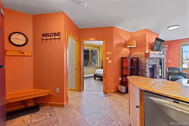 kitchen featuring dishwasher, light stone counters, a fireplace, and baseboards