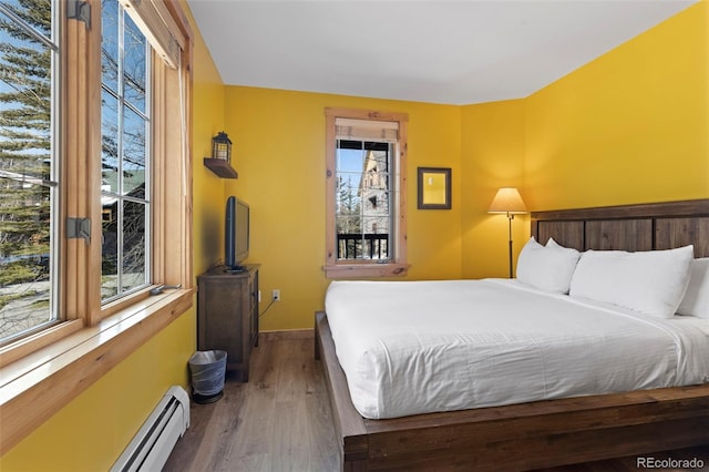 bedroom featuring a baseboard heating unit, baseboards, and wood finished floors