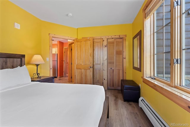 bedroom with visible vents, a baseboard heating unit, freestanding refrigerator, wood finished floors, and a closet