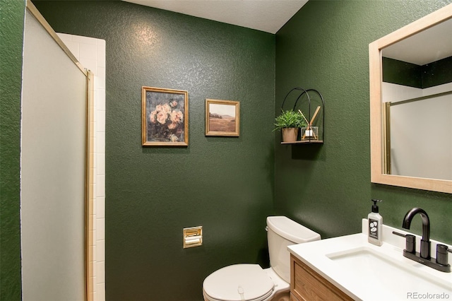 bathroom with a textured wall, toilet, vanity, and a shower with door