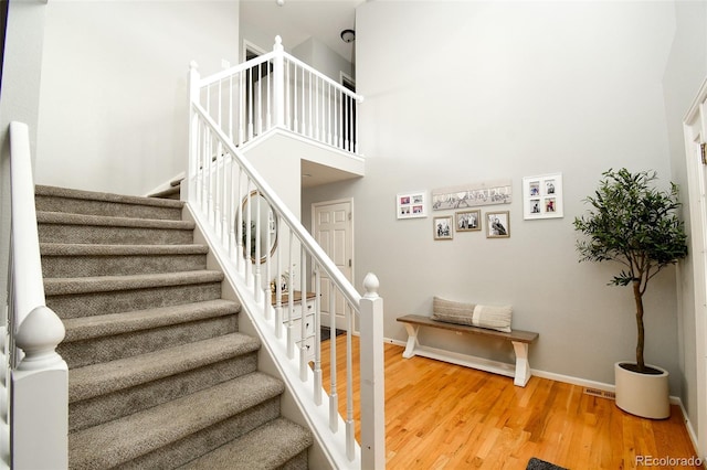 stairway with baseboards, a towering ceiling, and wood finished floors