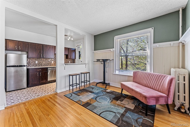 sitting room with a textured ceiling, light wood-type flooring, radiator heating unit, and baseboards