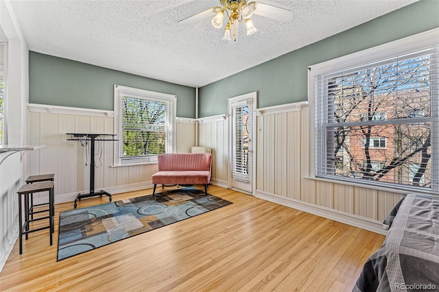 living area with ceiling fan, wood finished floors, a wainscoted wall, and a textured ceiling