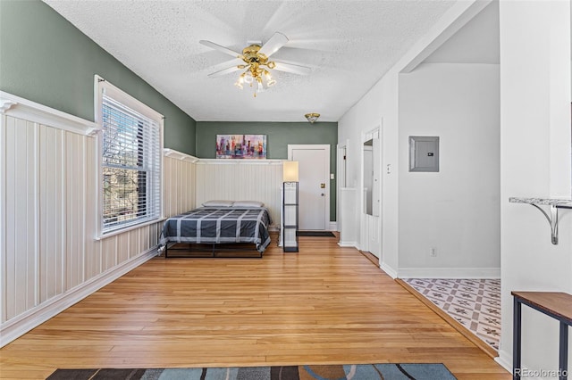 bedroom featuring ceiling fan, baseboards, electric panel, wood finished floors, and a textured ceiling