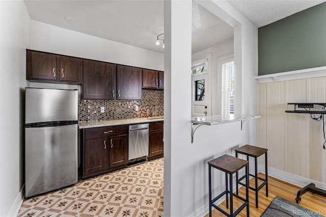 kitchen featuring dark brown cabinetry, light stone countertops, light floors, and appliances with stainless steel finishes